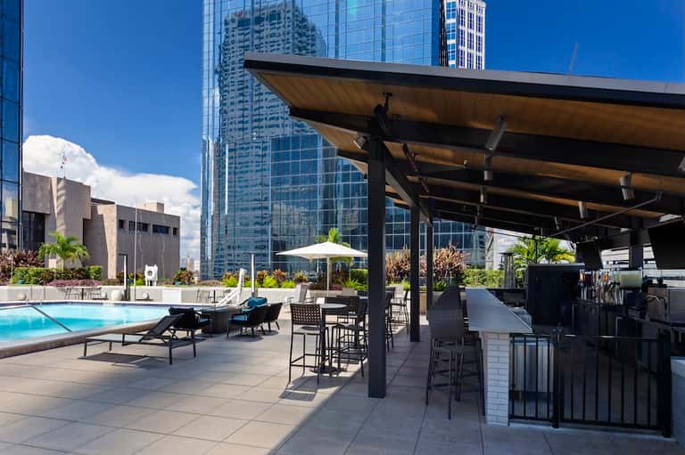Rooftop pool terrace with loungers, pergola, bar seating, and downtown city skyline views