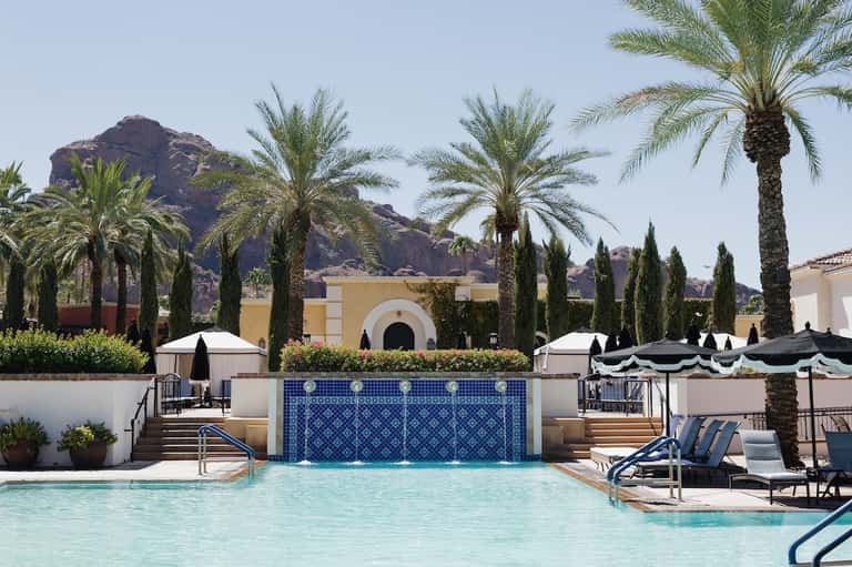 Resort pool with decorative blue tile waterfall, palm trees, and desert mountain backdrop