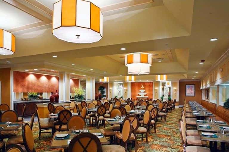 Elegant ballroom with round tables set for dining, orange striped lighting fixtures, and formal place settings