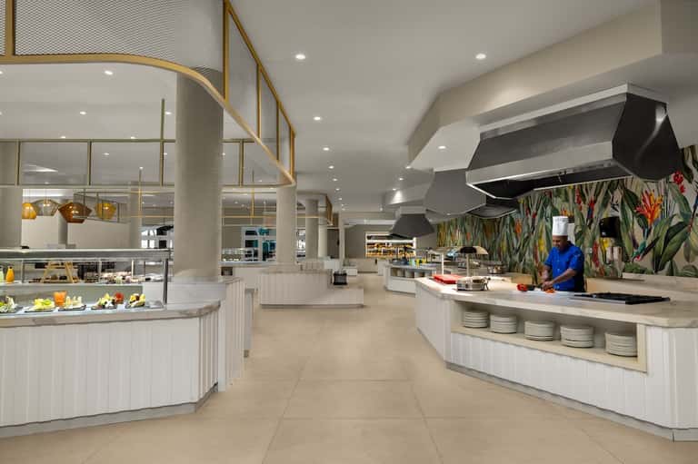 Modern hotel restaurant with white counters, botanical wallpaper, pendant lights, and open kitchen