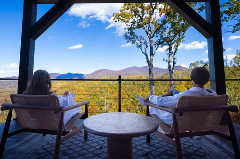Two guests relaxing on lounge chairs on mountain overlook patio with scenic valley landscape view