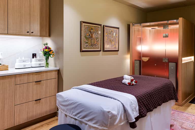 Spa treatment room with massage bed, wood cabinetry, and modern amenities