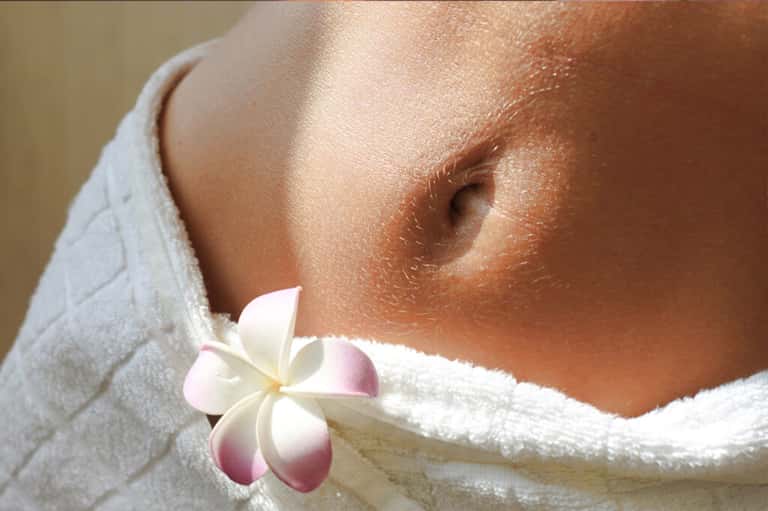 Spa setting showing person wrapped in white towel with plumeria flower accent