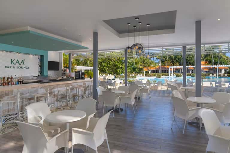 Modern bar and lounge area overlooking resort pool, white contemporary furniture, turquoise accent bar
