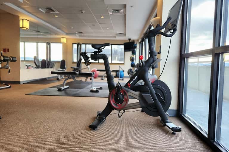 Fitness center with stationary exercise bike, dumbbells, equipment, and floor-to-ceiling windows overlooking water