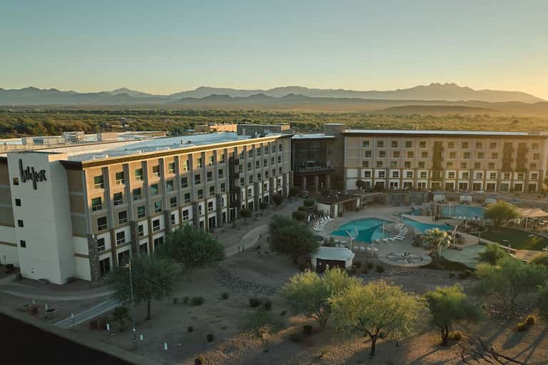 Modern hotel complex with pool area at sunset, desert landscape and mountains visible