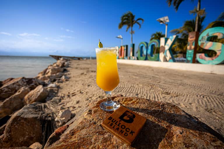 Tropical beach with colorful art installation, ocean view, palm trees, and yellow cocktail on sand