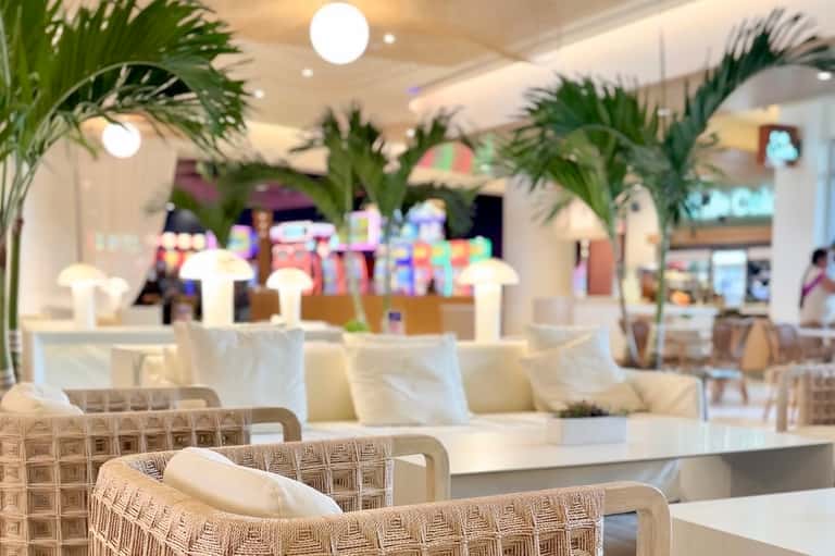 Upscale restaurant dining area with palm plants, white napkins, ambient lighting, and modern furnishings