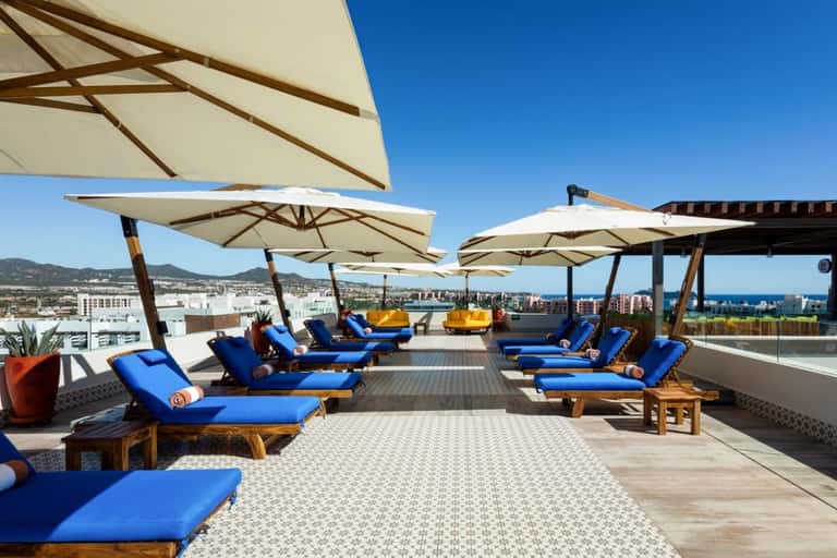 Rooftop lounge with lounge chairs, umbrellas, city skyline view, and modern landscape design