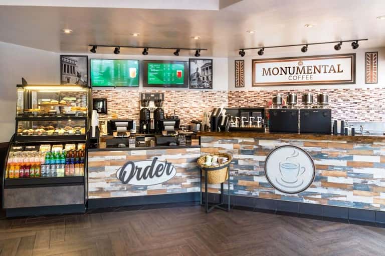 Bright coffee shop counter with Monumental Coffee signage, pastry display, menu boards, and service area