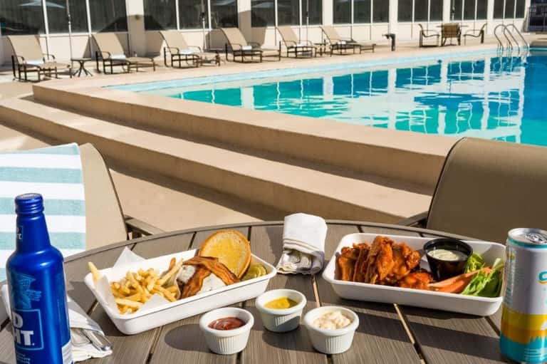 Pool deck with loungers, food and drinks on table, and lap pool in background