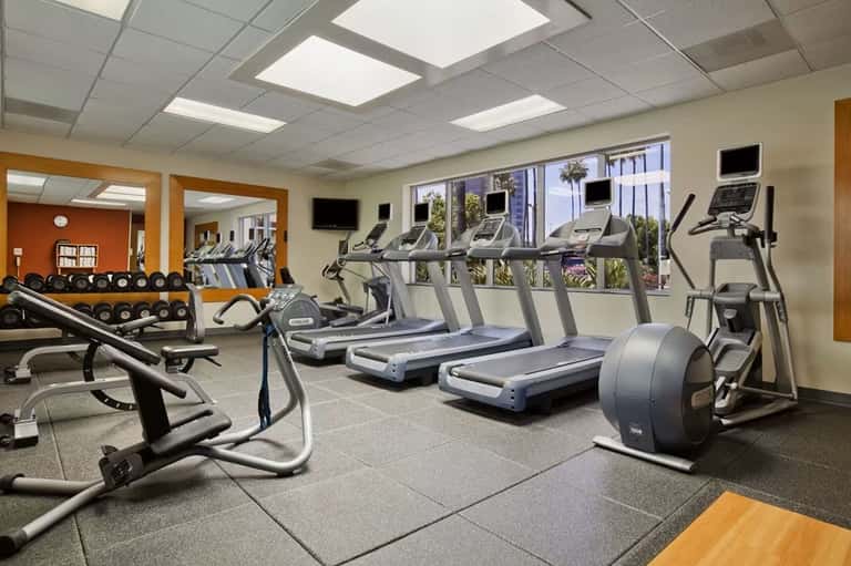 Hotel fitness center with treadmills, exercise bikes, dumbbells, and floor-to-ceiling windows