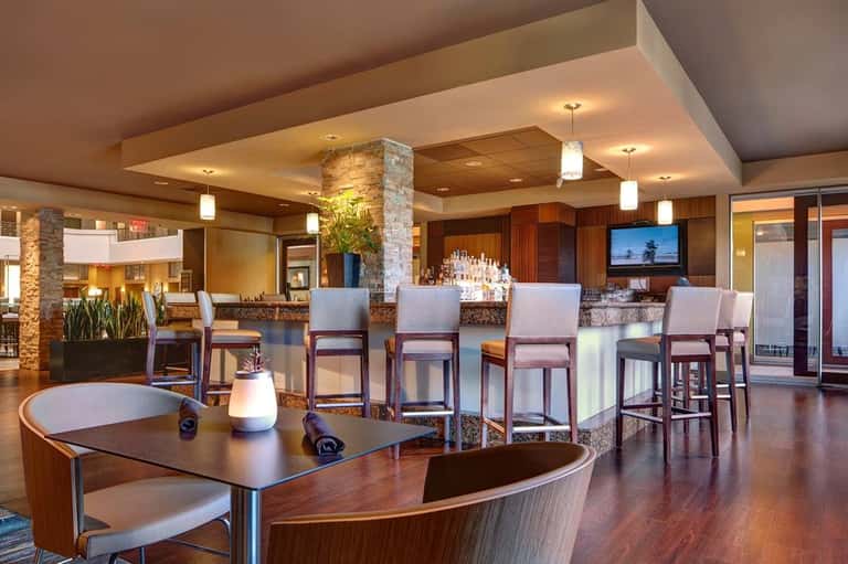 Modern hotel bar and lounge with stone accents, wood cabinetry, granite countertops, and floor-to-ceiling windows