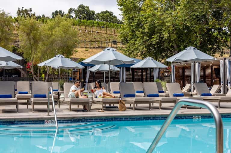Resort pool area with loungers, white umbrellas, vineyard view, and dining cabanas