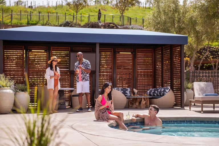 Group relaxing by resort pool with modern cabana and louvered privacy screens