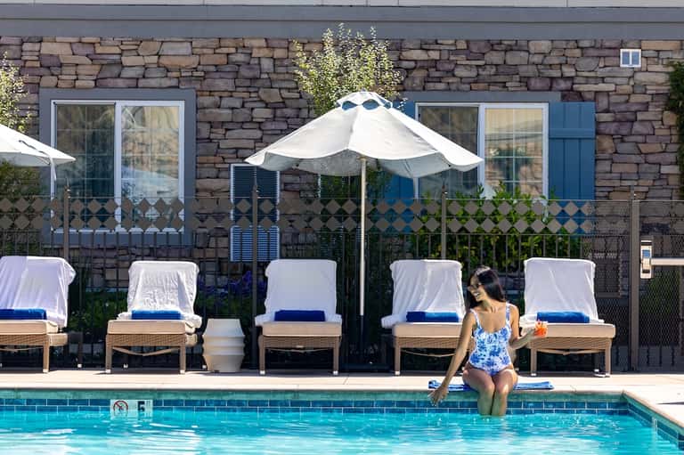 Resort pool with loungers under white umbrellas, stone building facade, and guest in water