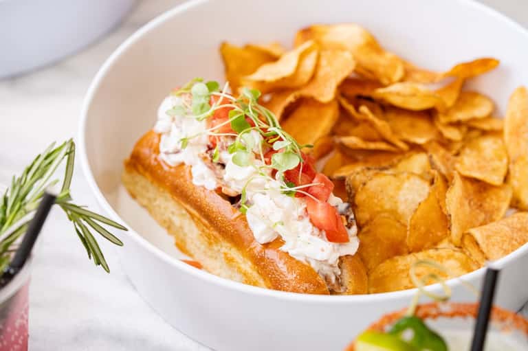 Gourmet lobster roll sandwich with crispy potato chips on white plate