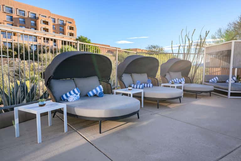 Rooftop daybeds with dark canopy covers, blue striped pillows, and urban building views