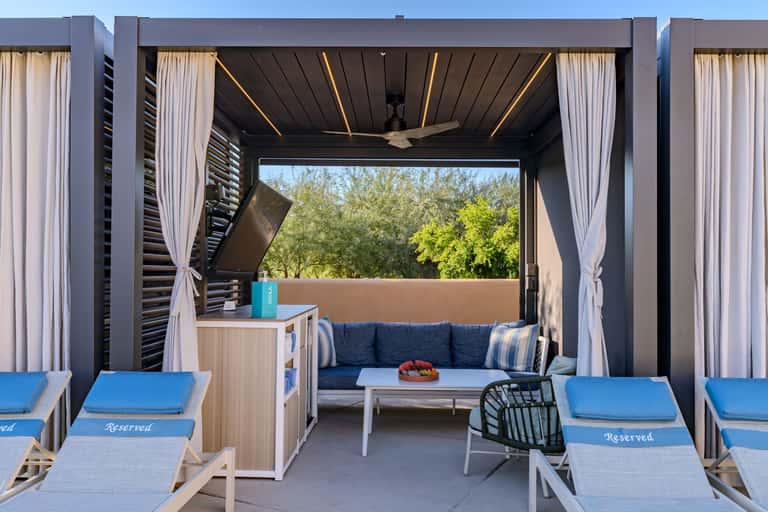 Covered poolside cabana with modern black pergola, blue seating, and ambient lighting