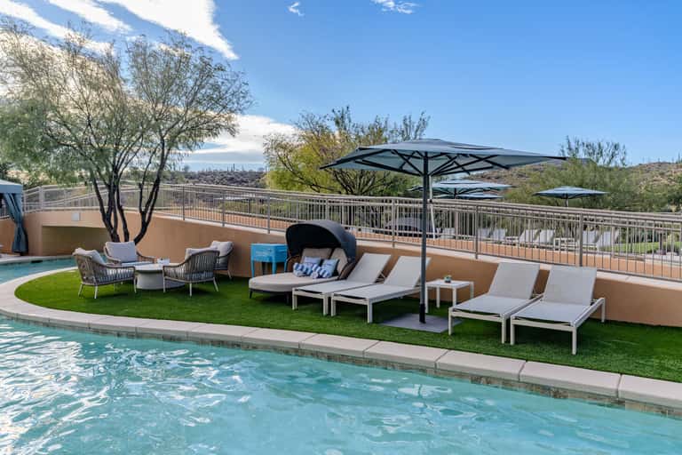 Luxury resort pool with artificial turf seating area, black umbrellas, desert landscape, and city skyline