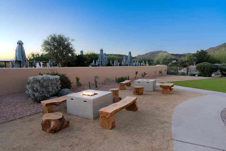 Fire pit gathering area with log seating, desert landscaping, and mountain backdrop
