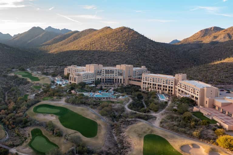 Aerial view of large resort nestled in desert mountains with pools and golf course