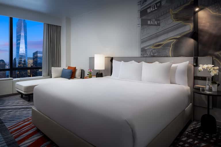 Luxury hotel bedroom with city skyline view, white bedding, and modern furnishings