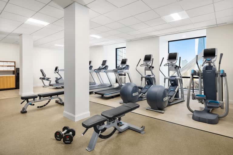 Modern fitness center with cardio equipment, free weights, treadmills, and floor-to-ceiling windows with city view