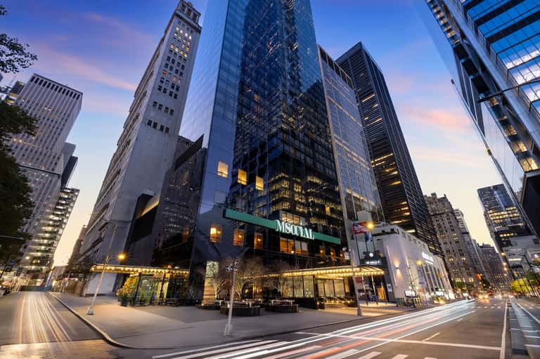 Modern glass and steel downtown office or hotel tower illuminated at dusk with street-level retail entrance
