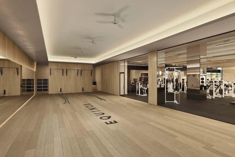 Modern gym with wood finishes, large mirrors, cardio equipment, and separate fitness machines area with glass partition