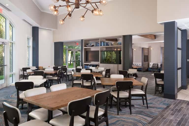 Modern hotel lobby lounge with wood tables, black chairs, shelving, and contemporary lighting