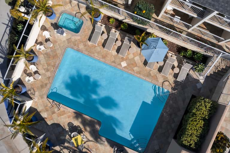 Aerial view of resort pools, sun loungers, umbrellas, palm trees, and beige terrace decking