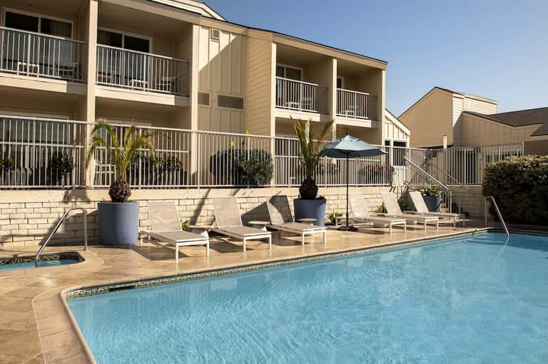Resort pool with lounge chairs, umbrellas, and multi-story residential buildings in background