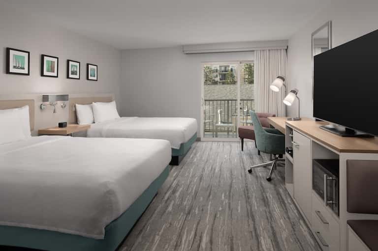 Hotel bedroom with two queen beds, desk area, and glass balcony door