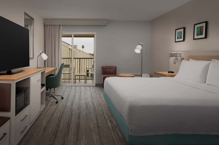Contemporary hotel room with queen bed, desk, flat-screen TV, balcony, and ocean view