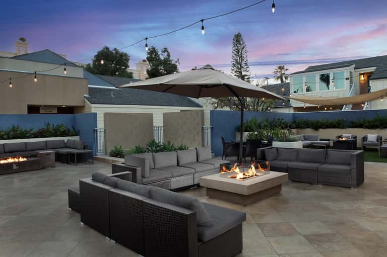 Upscale outdoor lounge at twilight with fire pits, rattan seating, and hanging string lights