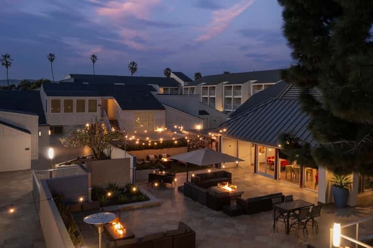 Illuminated resort courtyard at night with fire pits, lounge seating, and modern architecture