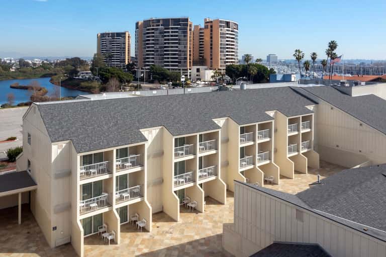 Beachfront row of cream-colored townhomes with balconies, overlooking marina and high-rise buildings