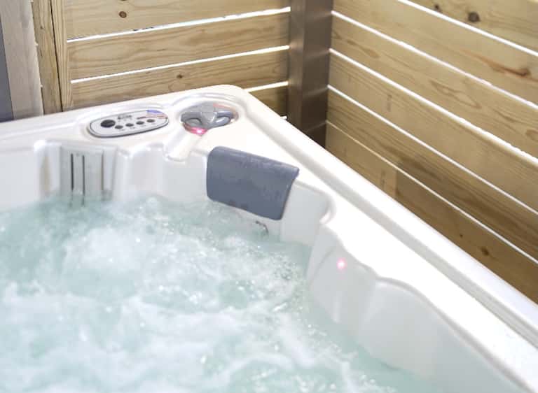Outdoor hot tub with white jets and controls, surrounded by wooden railings and water features