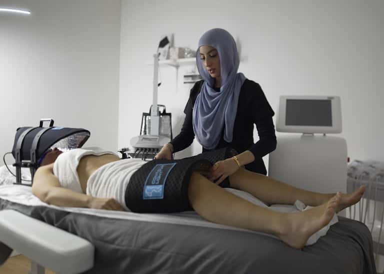 Technician performing electronic massage therapy on client's leg in modern wellness clinic