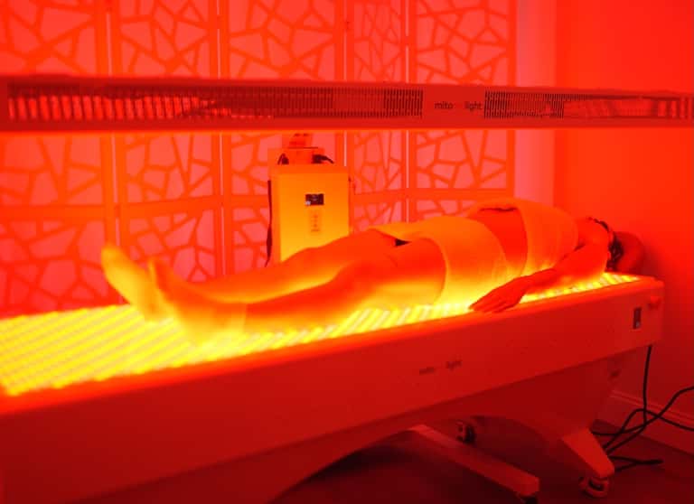 Red and yellow infrared light therapy bed with therapeutic tunnel design for wellness treatments at spa