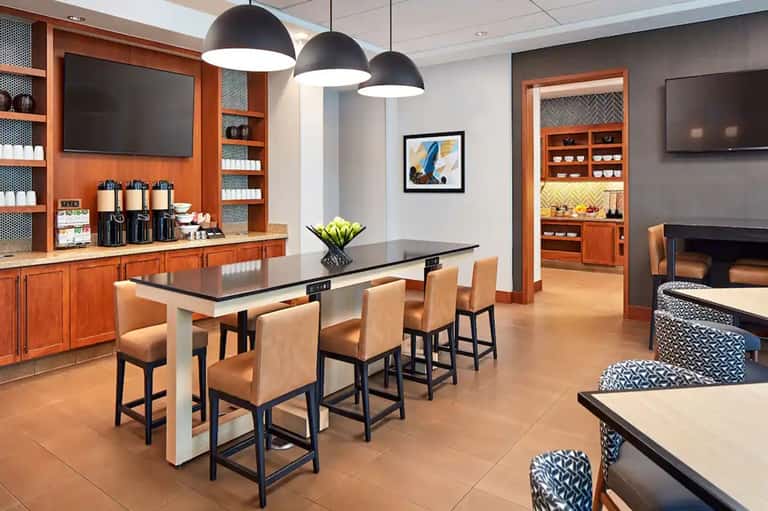 Modern resort lounge with high-top dining table, orange cabinetry, pendant lighting, and fireplace