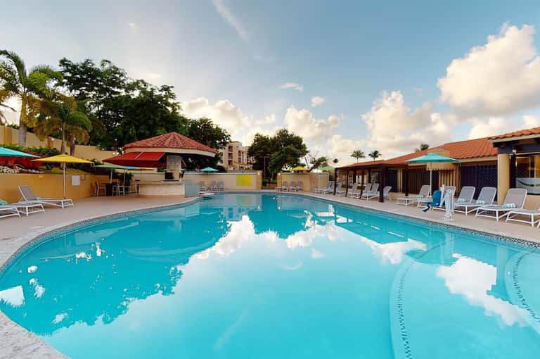 Resort swimming pool with turquoise water, lounge chairs, colorful umbrellas, and tropical landscaping