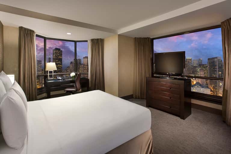 Luxury high-rise hotel room with city skyline views through floor-to-ceiling windows and modern furnishings