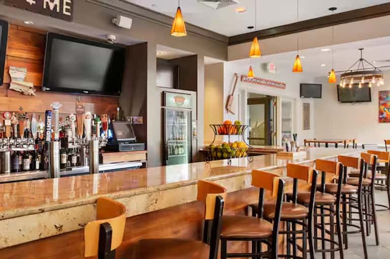 Casual sports bar dining area with orange seating, full bar counter, and pendant lighting