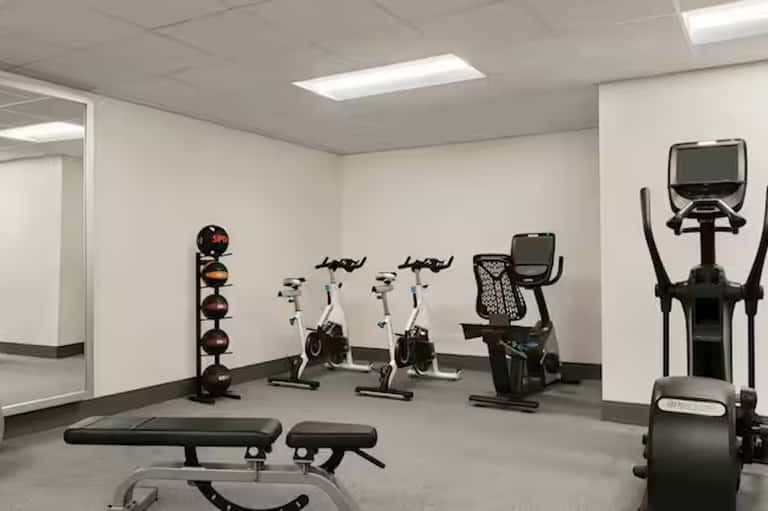 Compact fitness room with exercise bikes, weight rack, bench, and elliptical machine