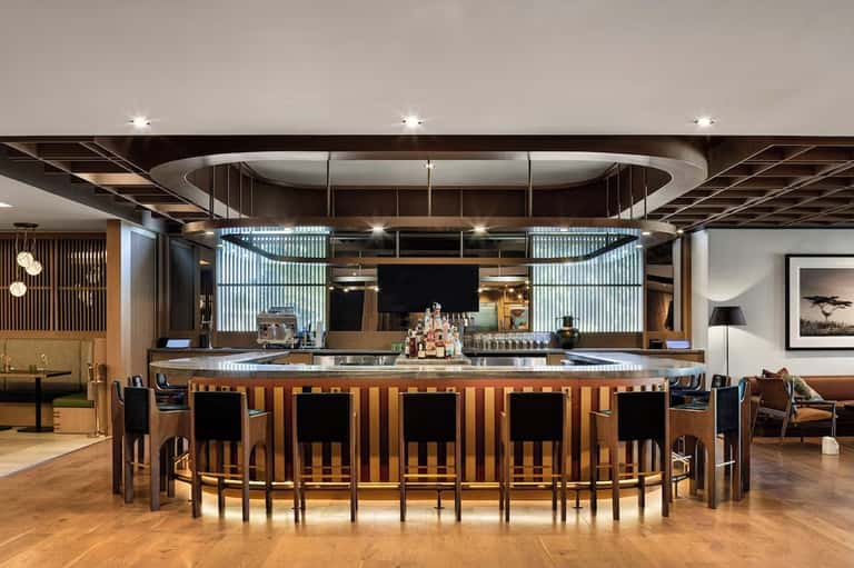 Modern hotel bar with curved wooden counter, glass panels, and contemporary lighting