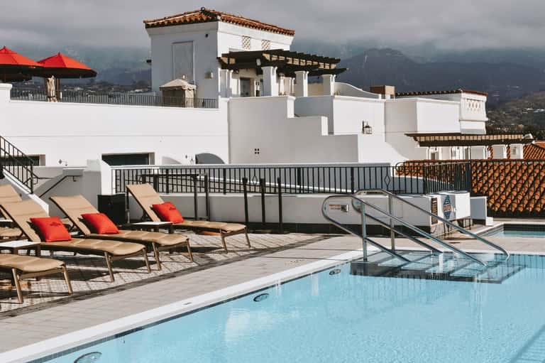 Hilltop resort pool with mountain views, lounge chairs with red cushions, and white architecture