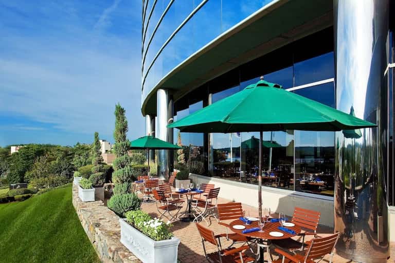 Elevated patio dining area with green umbrellas, orange chairs, and manicured lawn