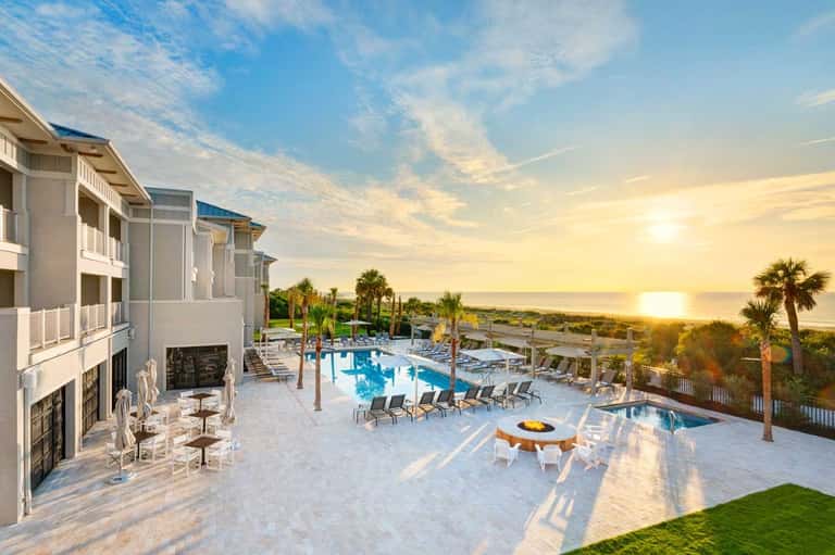 Oceanfront resort at sunset with pool, palm trees, fire pit, and coastal landscape views